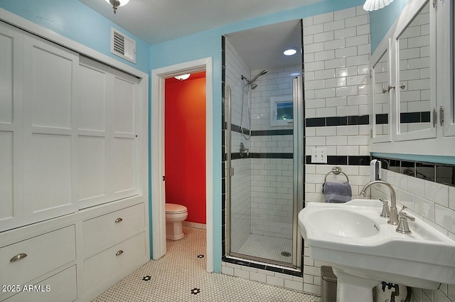 bathroom with toilet, tile walls, tile patterned floors, sink, and a shower with door