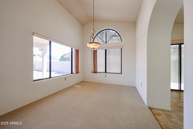 spare room with arched walkways, light carpet, and high vaulted ceiling