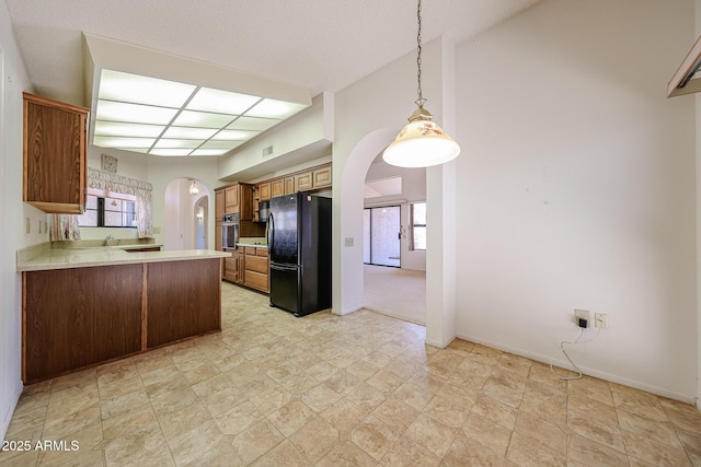 kitchen with freestanding refrigerator, a peninsula, stainless steel oven, light countertops, and arched walkways