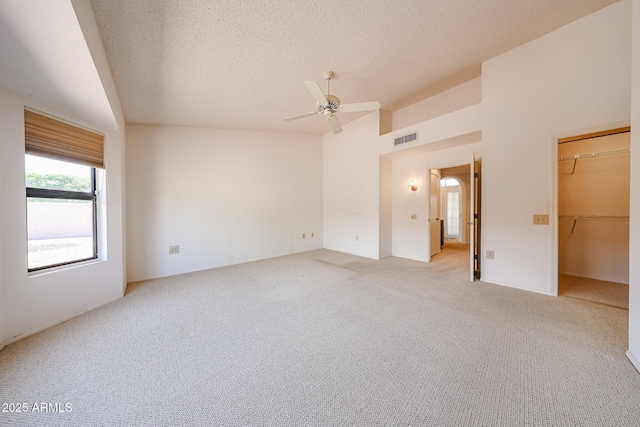 unfurnished room featuring a ceiling fan, a textured ceiling, light colored carpet, visible vents, and vaulted ceiling