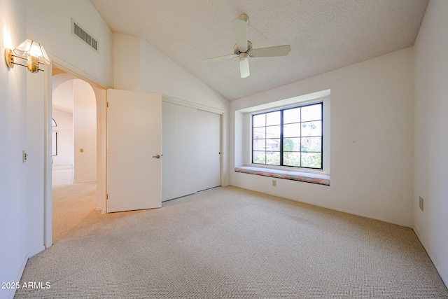 unfurnished bedroom with visible vents, arched walkways, a closet, lofted ceiling, and carpet flooring
