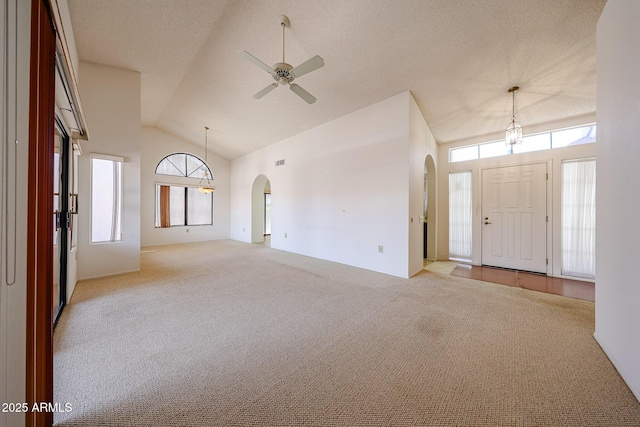 foyer entrance with visible vents, lofted ceiling, ceiling fan, light colored carpet, and arched walkways
