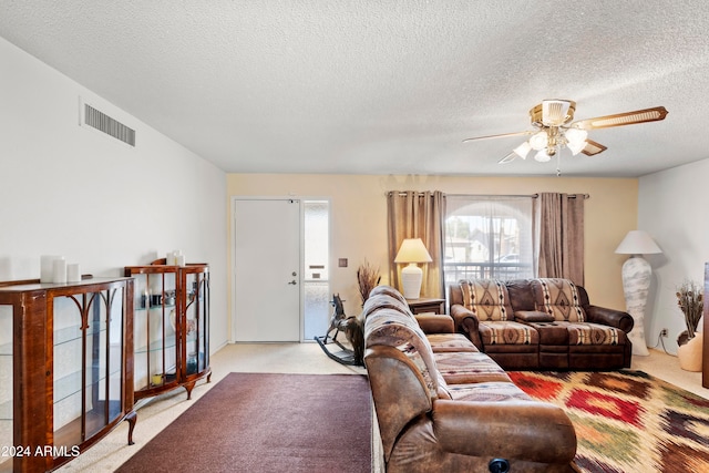 living room featuring ceiling fan, visible vents, a textured ceiling, and light colored carpet