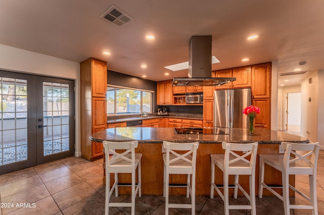 kitchen featuring french doors, a spacious island, appliances with stainless steel finishes, a kitchen bar, and island exhaust hood