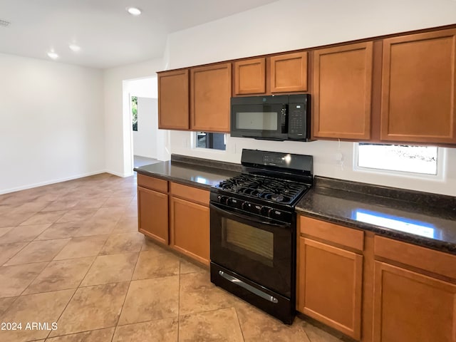 kitchen featuring light tile patterned flooring, dark stone counters, and black appliances