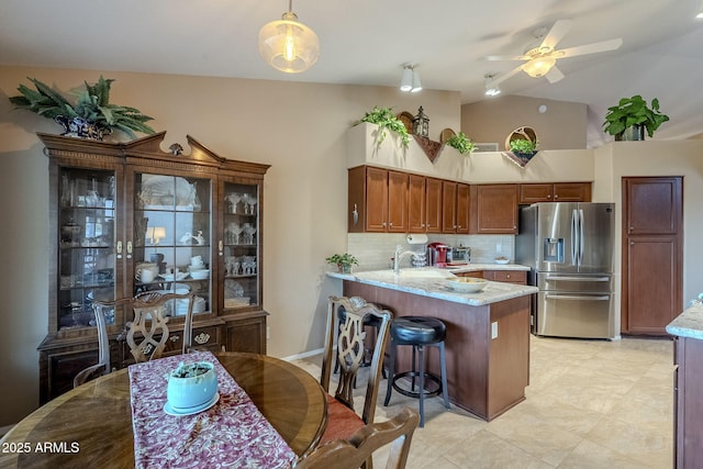 kitchen featuring backsplash, kitchen peninsula, light stone countertops, decorative light fixtures, and stainless steel fridge with ice dispenser