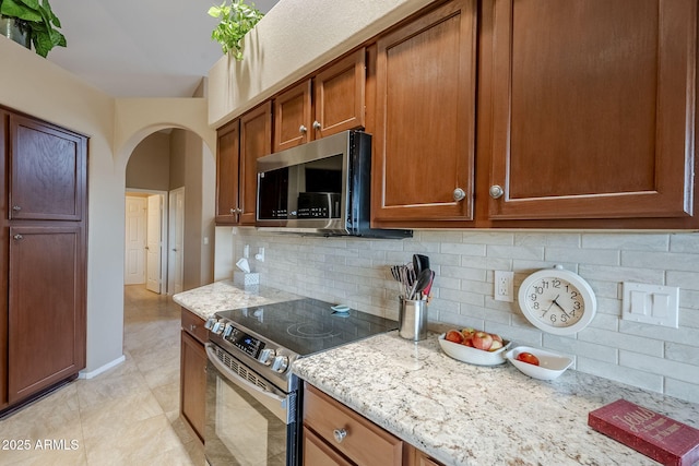 kitchen featuring tasteful backsplash, light stone countertops, light tile patterned floors, and appliances with stainless steel finishes