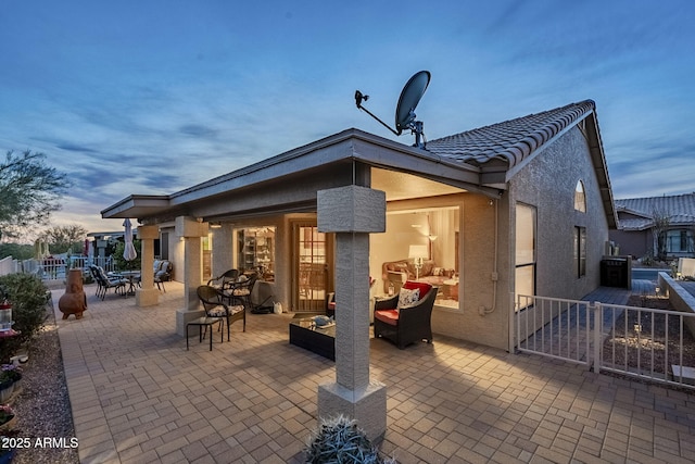 back house at dusk with outdoor lounge area and a patio