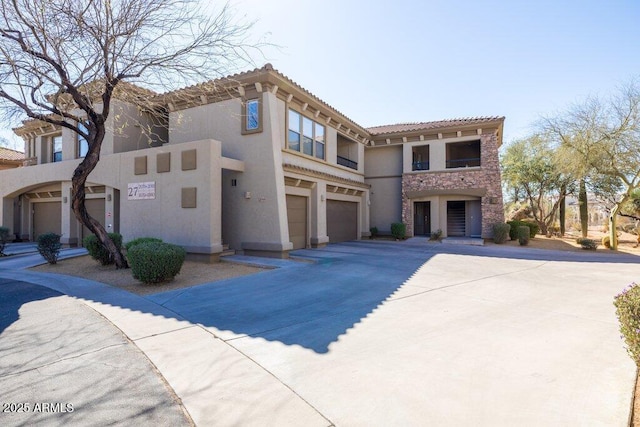 mediterranean / spanish-style home with an attached garage, concrete driveway, stone siding, a tiled roof, and stucco siding