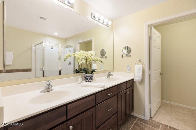 full bathroom with double vanity, a stall shower, visible vents, and a sink