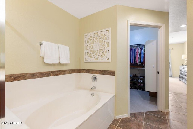 bathroom with a spacious closet, a bath, and tile patterned floors