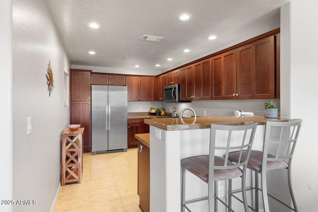 kitchen featuring visible vents, appliances with stainless steel finishes, a kitchen breakfast bar, a peninsula, and a textured ceiling