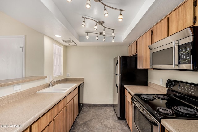 kitchen featuring stainless steel appliances, light countertops, a tray ceiling, and a sink