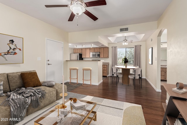 living area with dark wood-type flooring, a ceiling fan, visible vents, and baseboards