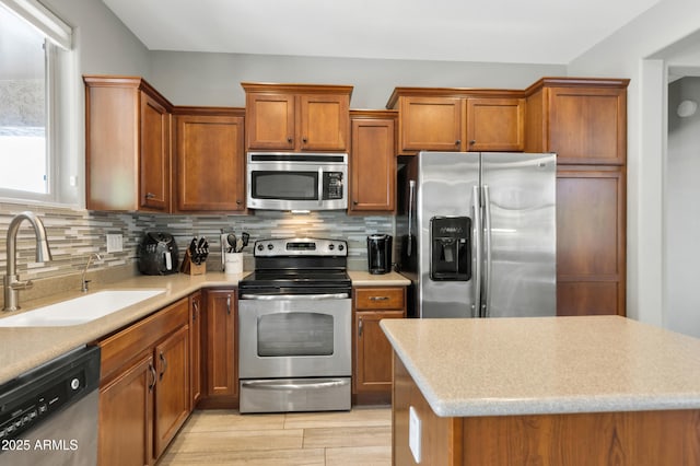 kitchen with stainless steel appliances, a sink, brown cabinets, backsplash, and light wood-type flooring