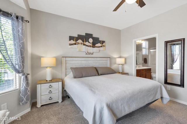 carpeted bedroom with multiple windows, ensuite bath, baseboards, and a ceiling fan