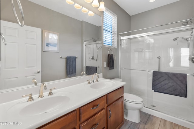 bathroom with a shower stall, double vanity, toilet, and wood finished floors