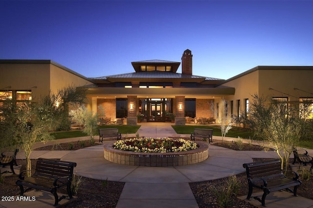rear view of property featuring a standing seam roof, a chimney, an outdoor fire pit, metal roof, and a patio area