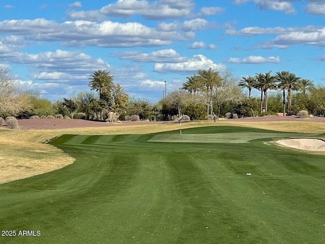 view of community featuring view of golf course, a putting green, and view of wooded area