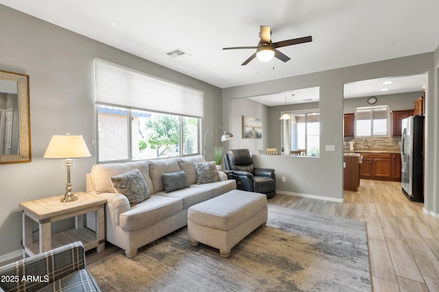 living area featuring a ceiling fan, light wood-style floors, and baseboards