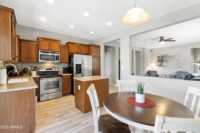 kitchen with stainless steel appliances, a sink, light countertops, backsplash, and brown cabinets