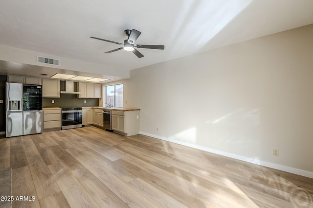 kitchen featuring appliances with stainless steel finishes, light wood-type flooring, ceiling fan, wall chimney range hood, and cream cabinetry