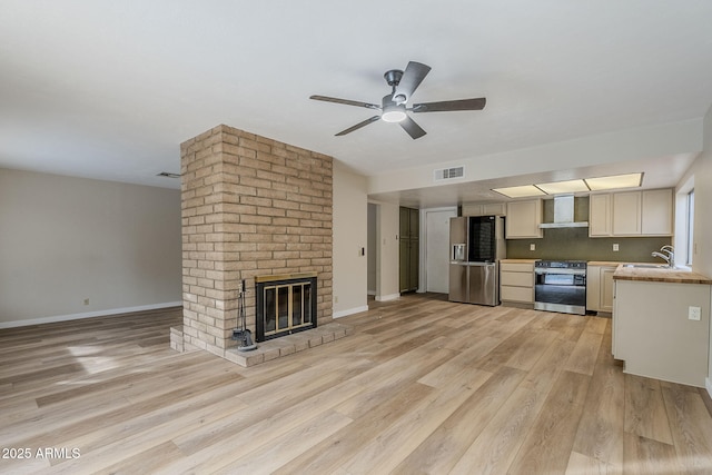 unfurnished living room with light wood-type flooring, a brick fireplace, ceiling fan, and sink