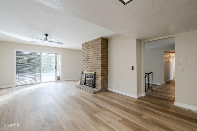 unfurnished living room with a textured ceiling, hardwood / wood-style flooring, a brick fireplace, and ceiling fan