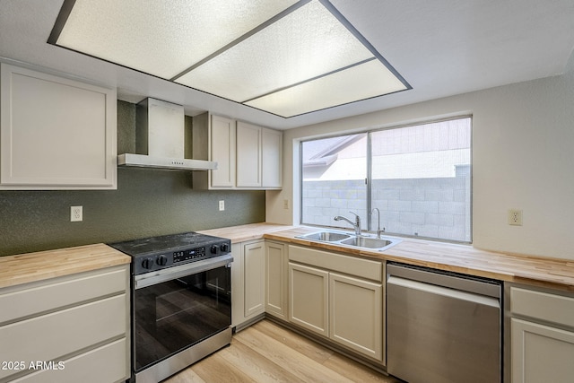 kitchen featuring sink, wall chimney exhaust hood, stainless steel appliances, wooden counters, and light wood-type flooring