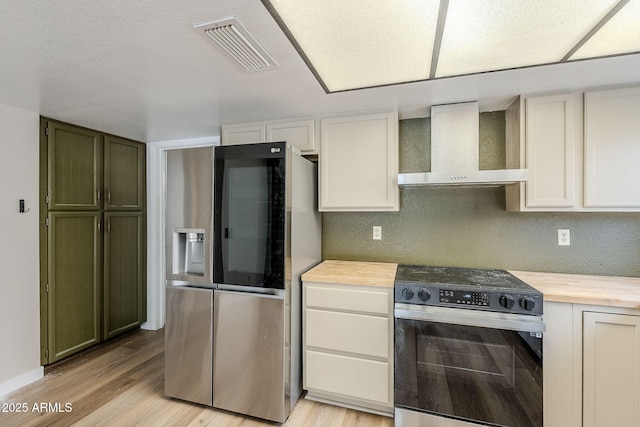 kitchen featuring butcher block countertops, white cabinets, wall chimney range hood, and appliances with stainless steel finishes