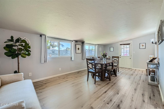 dining area featuring a textured ceiling, light hardwood / wood-style flooring, a wealth of natural light, and lofted ceiling