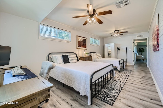 bedroom featuring ceiling fan, light hardwood / wood-style flooring, and brick wall