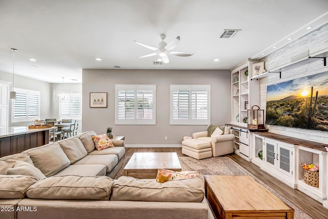 living room with built in shelves, ceiling fan with notable chandelier, and light wood-type flooring