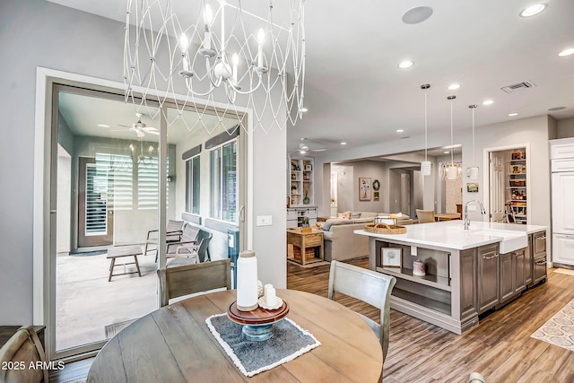 dining space with sink, ceiling fan with notable chandelier, and light wood-type flooring