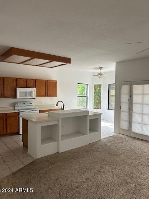 kitchen featuring ceiling fan, french doors, a kitchen island with sink, white appliances, and light carpet