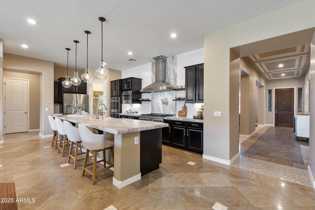 6918 E Ivyglen St, Mesa, AZ 85207 - kitchen with wall chimney range hood, stainless steel appliances, light countertops, dark cabinetry, and a large island with sink