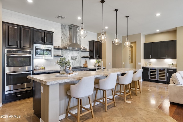 6918 E Ivyglen St, Mesa, AZ 85207 - kitchen featuring wall chimney exhaust hood, appliances with stainless steel finishes, wine cooler, backsplash, and a kitchen breakfast bar