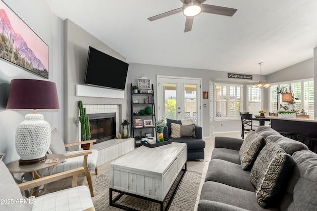 living room featuring a tiled fireplace, light tile patterned floors, baseboards, ceiling fan with notable chandelier, and lofted ceiling
