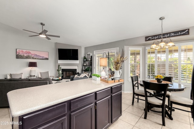 kitchen with hanging light fixtures, light countertops, a glass covered fireplace, ceiling fan with notable chandelier, and light tile patterned floors