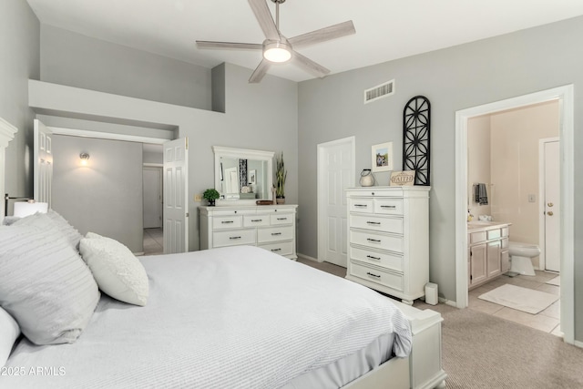 bedroom with visible vents, ensuite bathroom, light colored carpet, a ceiling fan, and light tile patterned floors