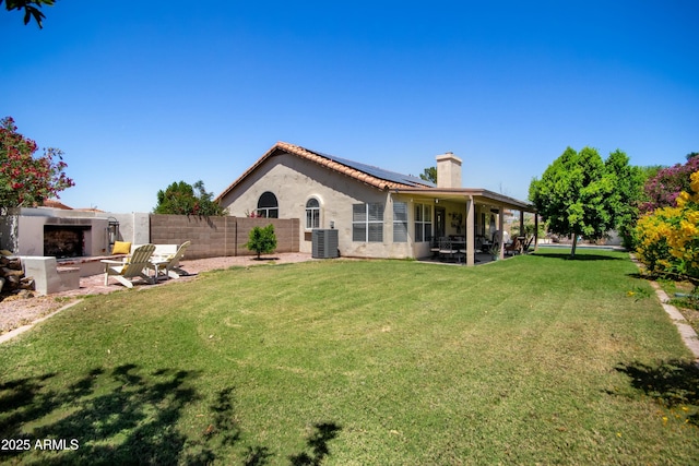 rear view of property with exterior fireplace, solar panels, a chimney, central AC, and a patio