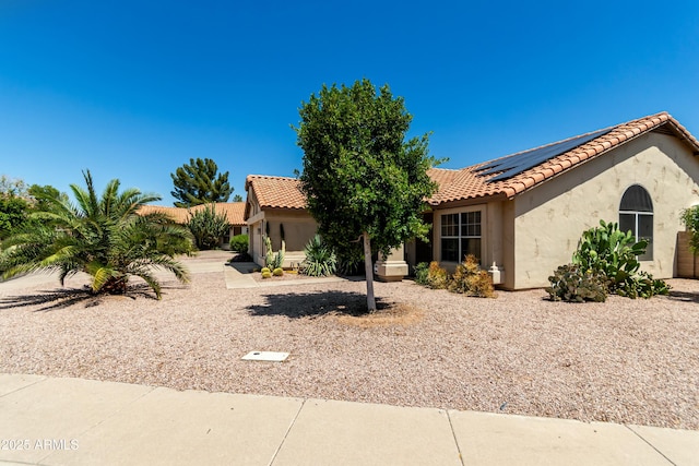 mediterranean / spanish-style home featuring stucco siding, solar panels, and a tiled roof