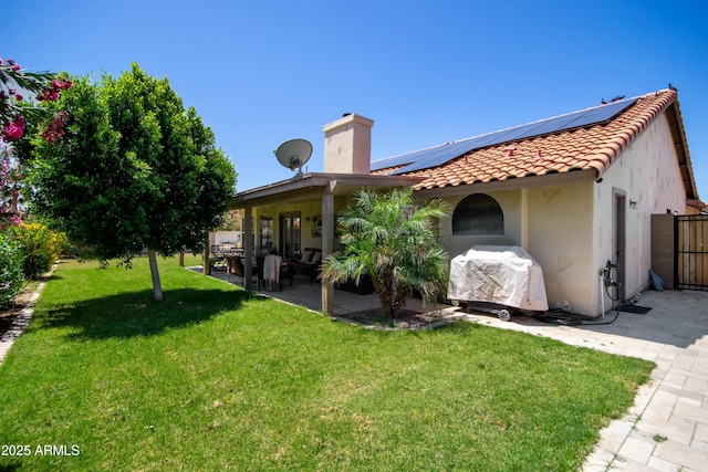 rear view of house with a chimney, a lawn, a patio area, roof mounted solar panels, and stucco siding