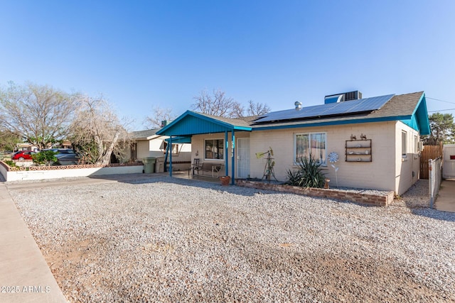 view of front of home with a patio area, roof mounted solar panels, and fence