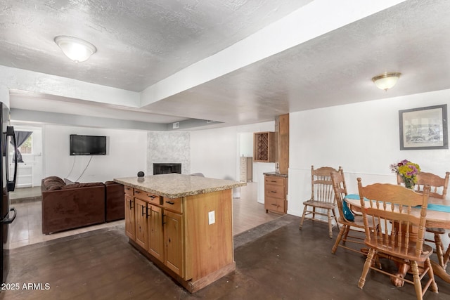 kitchen featuring a kitchen island, a textured ceiling, open floor plan, a fireplace, and concrete flooring