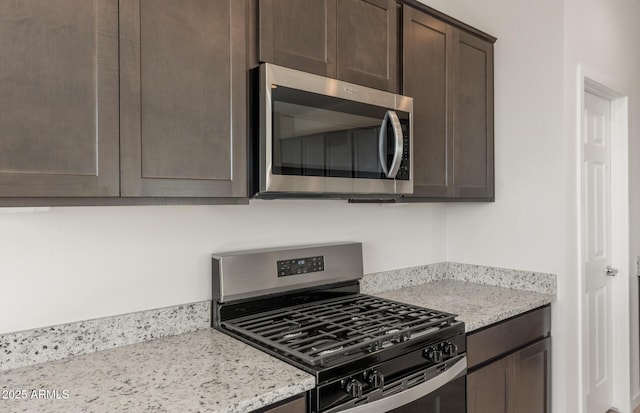 kitchen featuring light stone counters, dark brown cabinets, and stainless steel appliances