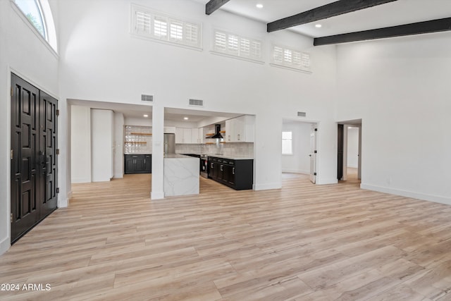 unfurnished living room with light wood-type flooring, plenty of natural light, and beamed ceiling