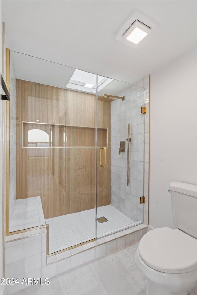 bathroom with walk in shower, a skylight, toilet, and tile patterned floors