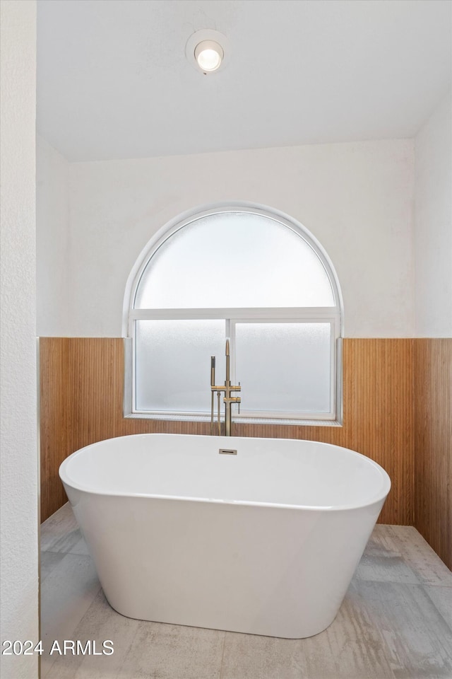 bathroom featuring a washtub, wooden walls, and a healthy amount of sunlight