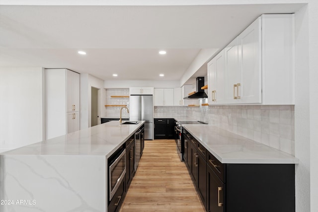 kitchen featuring light stone counters, stainless steel appliances, white cabinets, wall chimney exhaust hood, and light hardwood / wood-style flooring